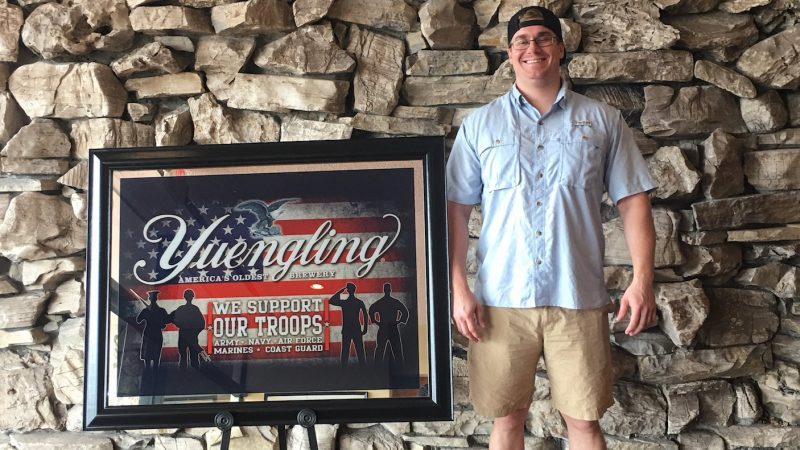 Scholarship recipient standing next to a patriotic Yuengling sign